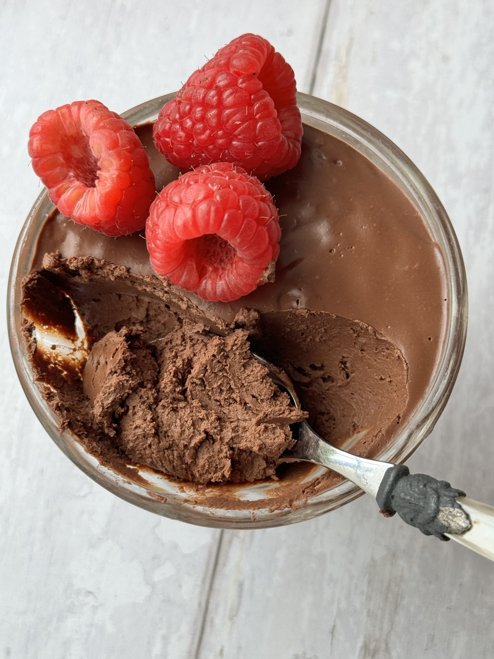 chocolate protein mousse in a glass coupe with raspberries on top and a spoon