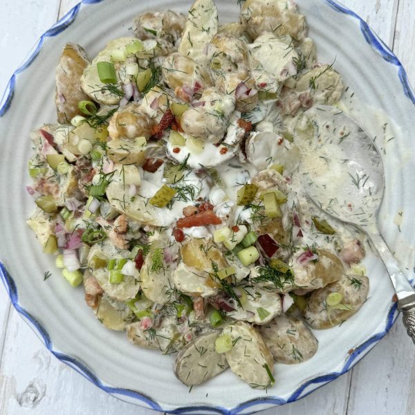 potato salad with dill pickles on a white plate with a spoon