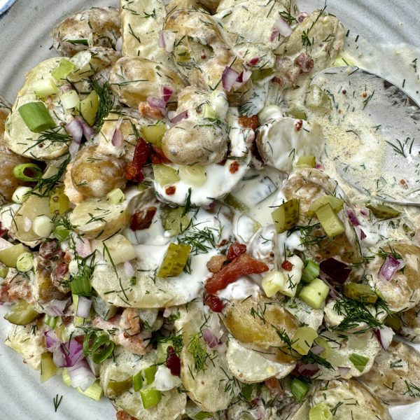 potato salad with dill pickles on a white plate with a spoon