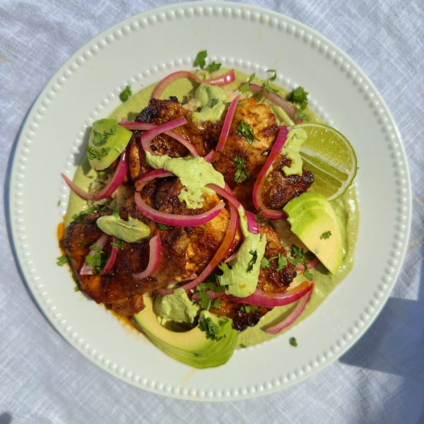 peruvian chicken in a white bowl topped with avocado and pink pickled onions