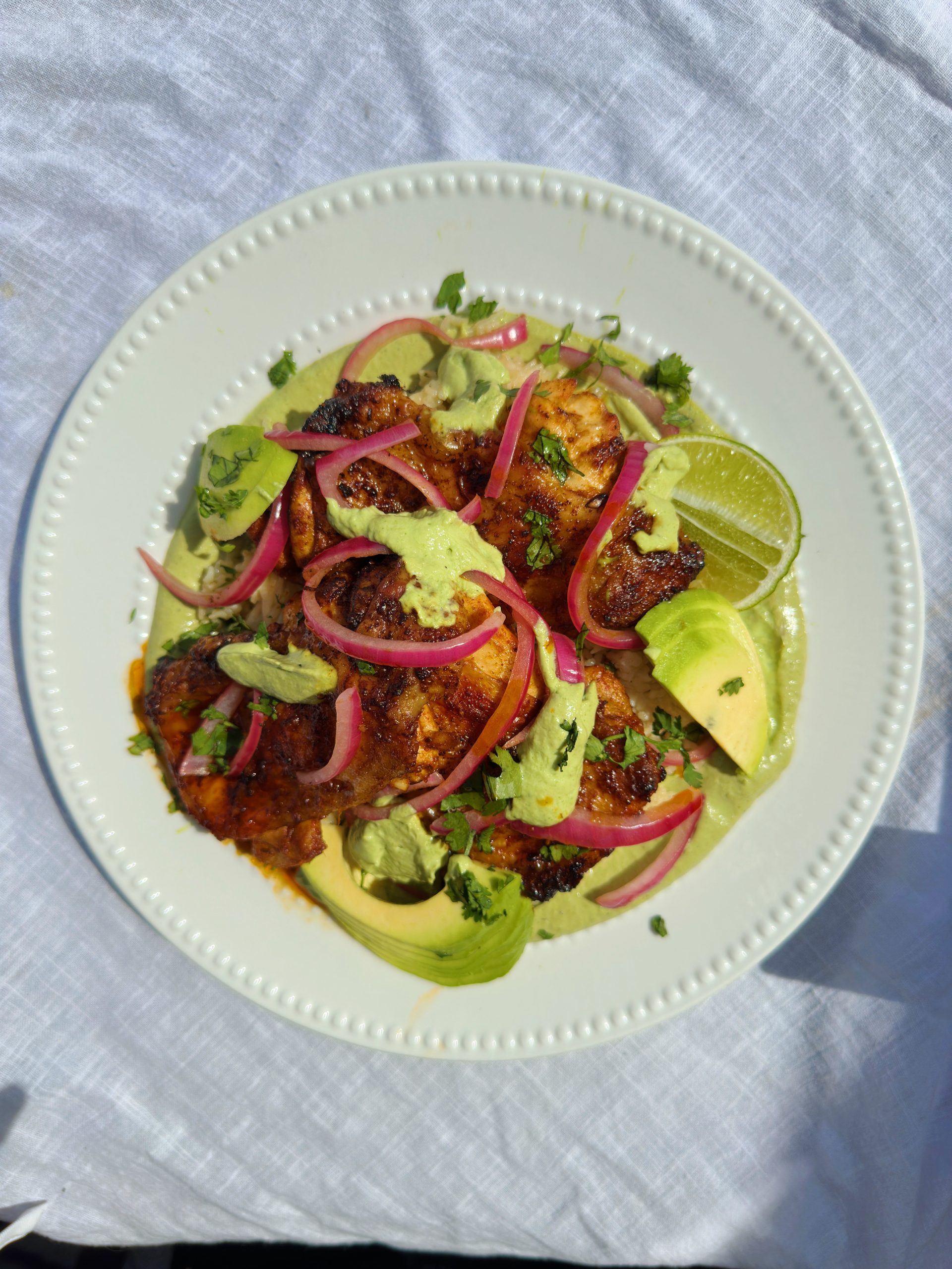 peruvian chicken in a white bowl topped with avocado and pink pickled onions