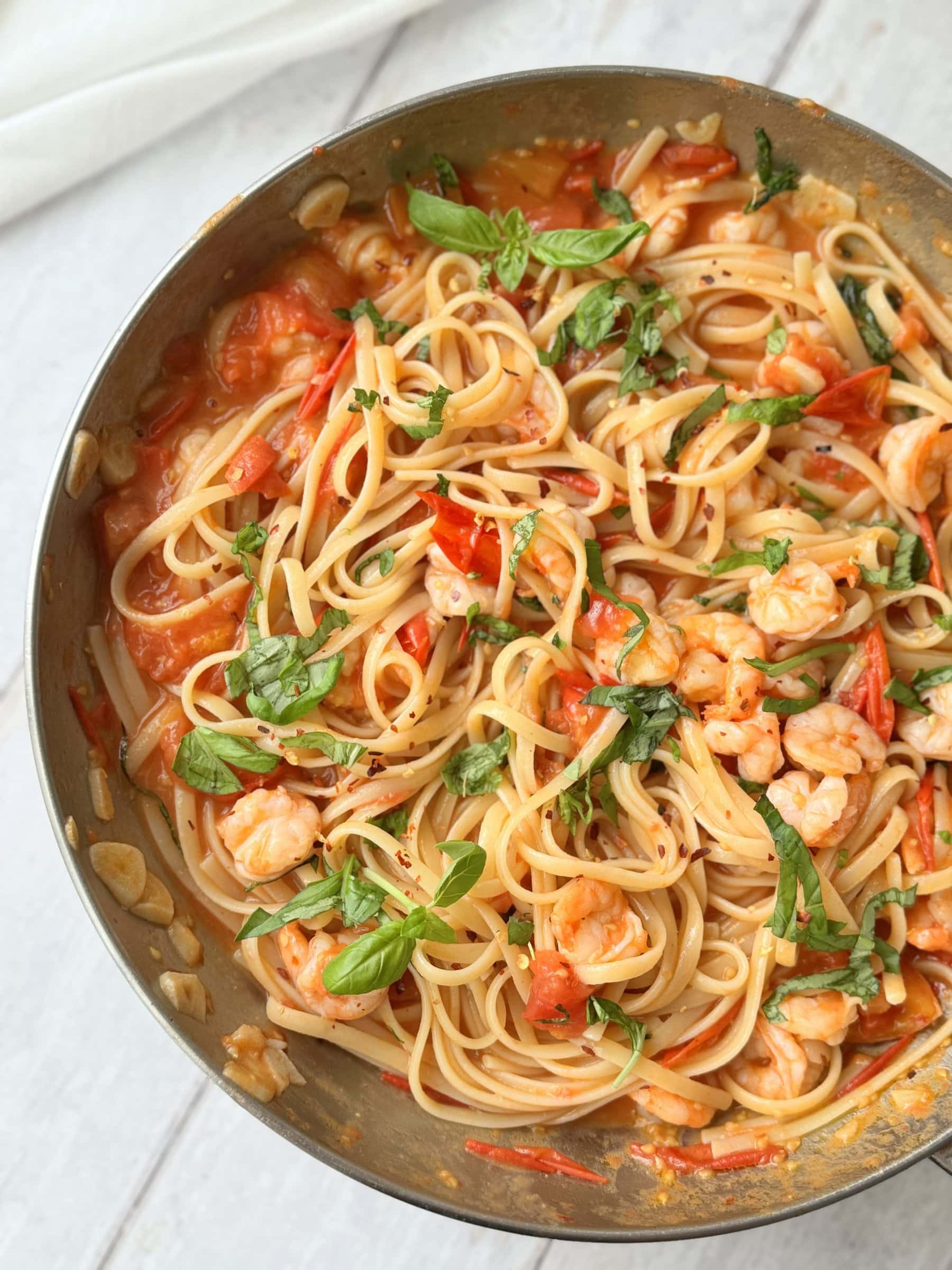 a pan of prawn tomato linguine on a white table