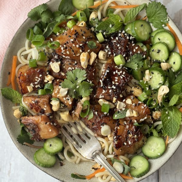 pork belly noodles in a white bowl decorated with herbs and cucumber