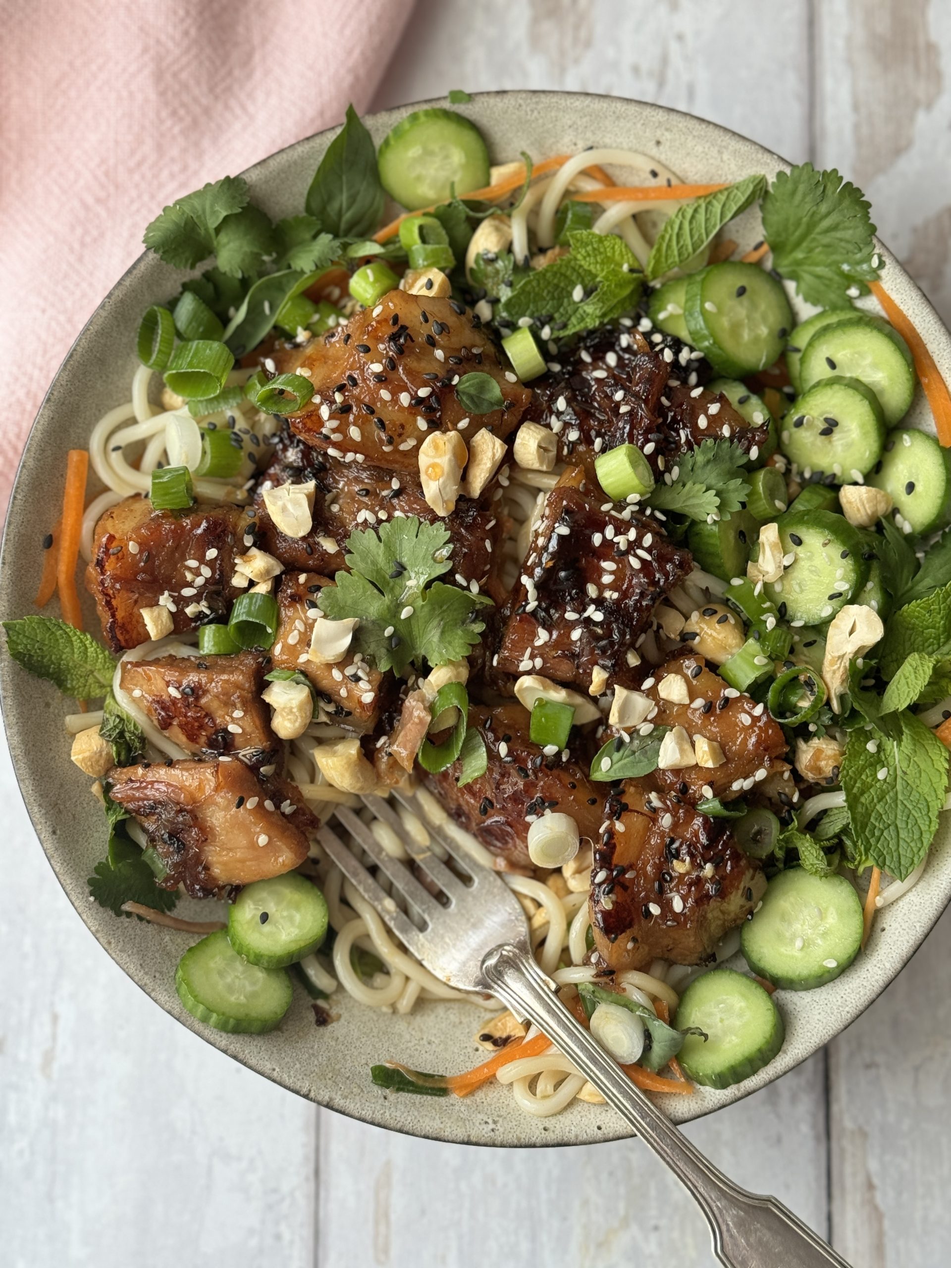 pork belly noodles in a white bowl decorated with herbs and cucumber