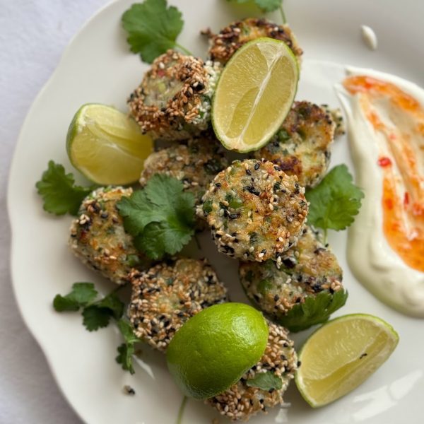 Plate of Thai Fish Cakes coated in sesame seeds served with spicy mayo, lime wedges and fresh coriander.