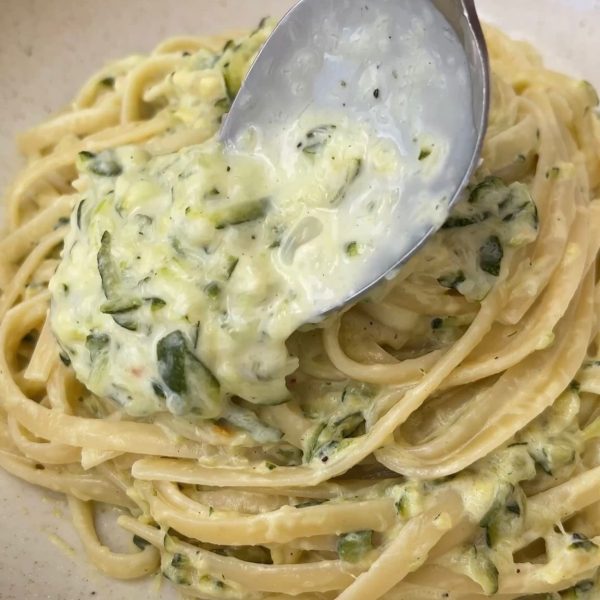 spooning sauce over courgette pasta in a beige bowl