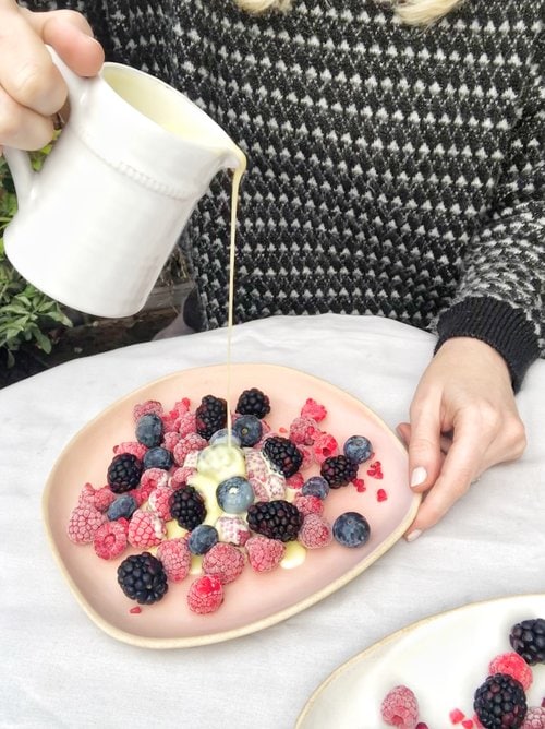 woman pouring white chocolate sauce on frozen berries