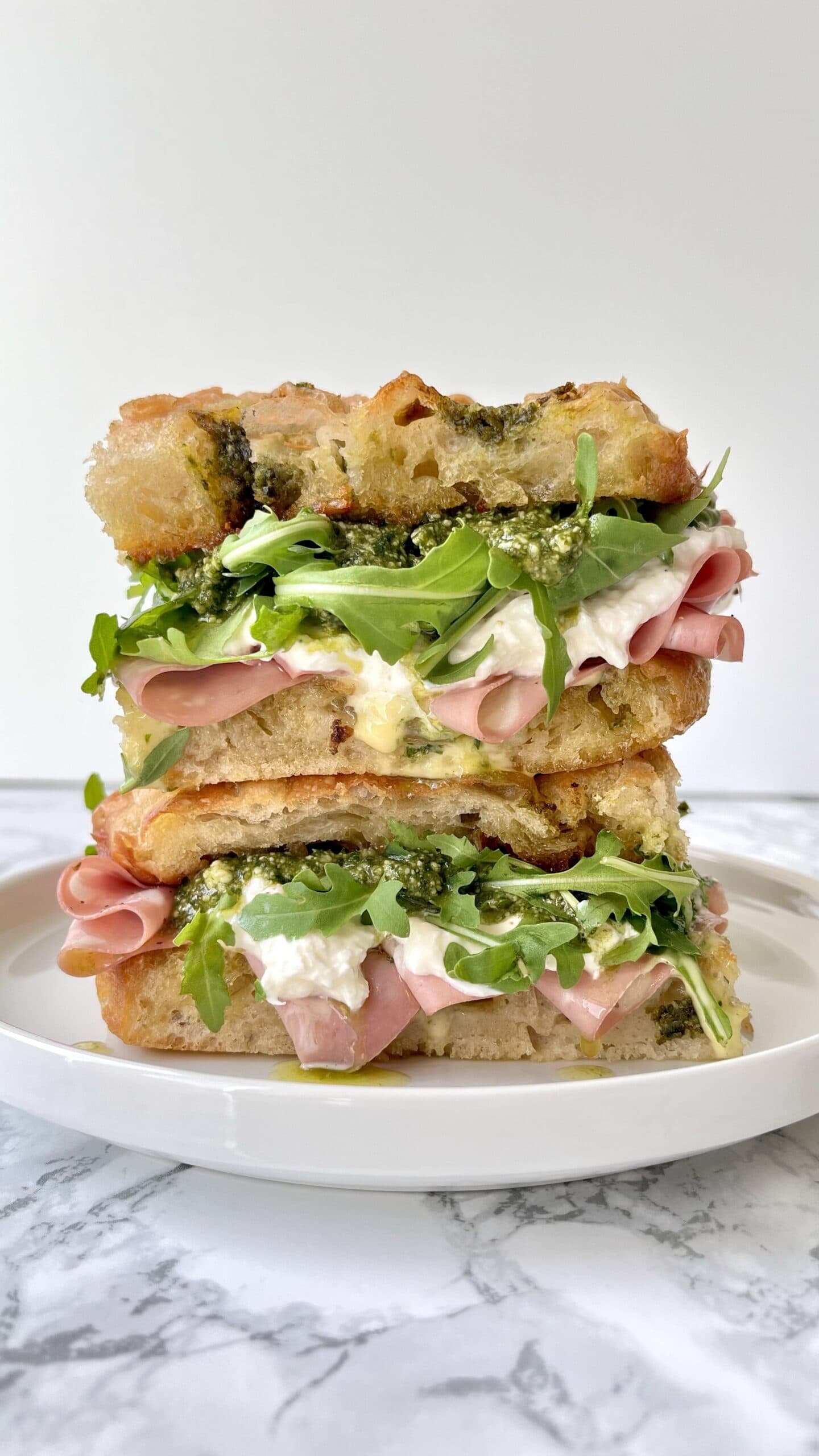 mortadella burrata sandwich with rocket, pesto, stacked on a plate