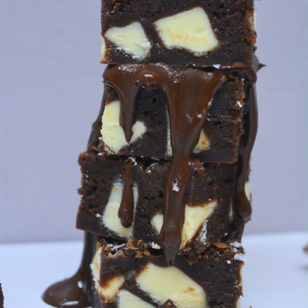 Stack of triple chocolate brownies with white chocolate chunks drizzled with melted dark chocolate.