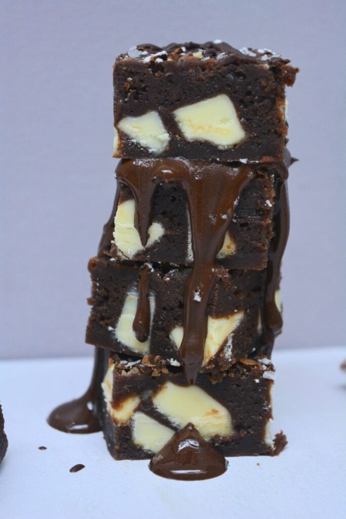 Stack of triple chocolate brownies with white chocolate chunks drizzled with melted dark chocolate.