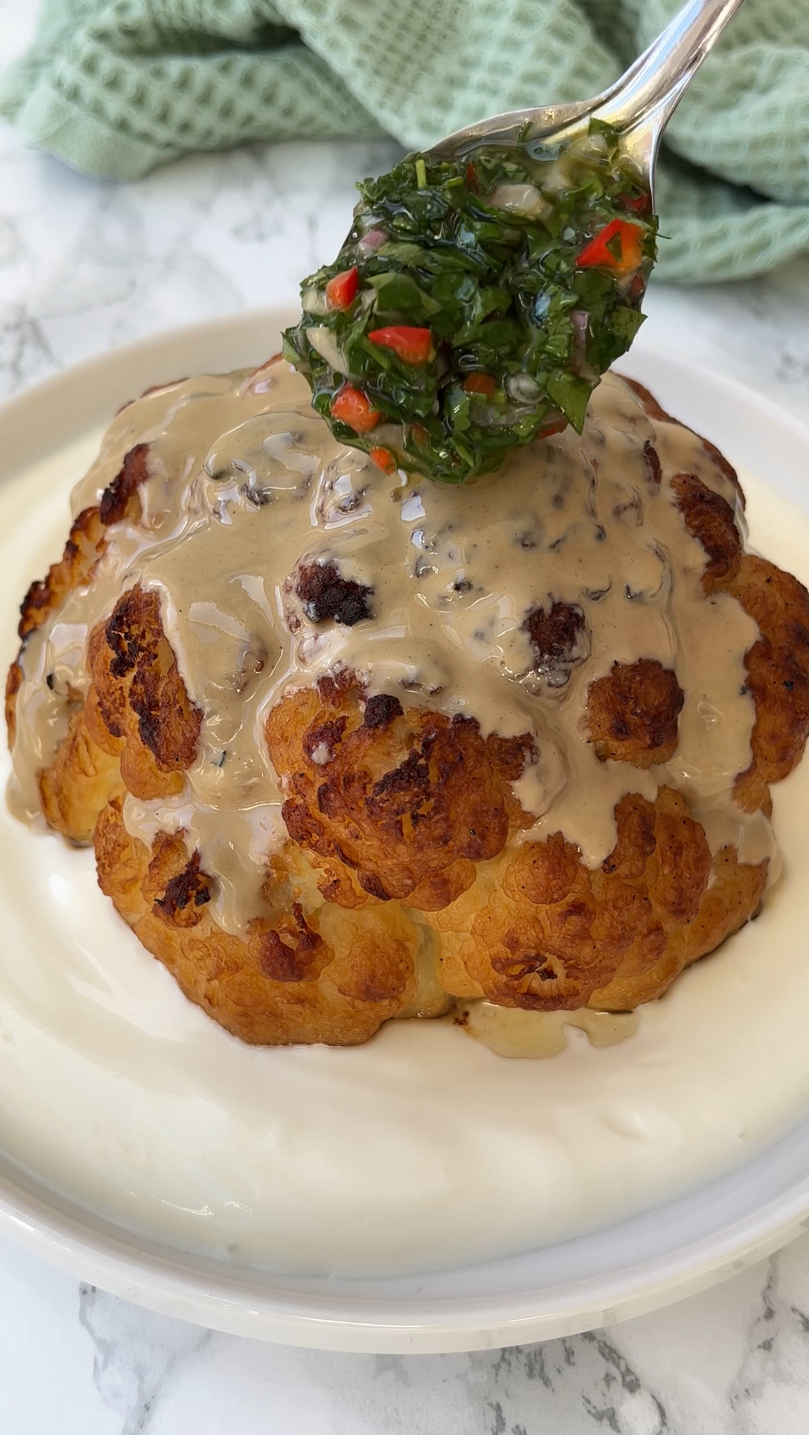 adding chimichurri to the tahini roasted cauliflower