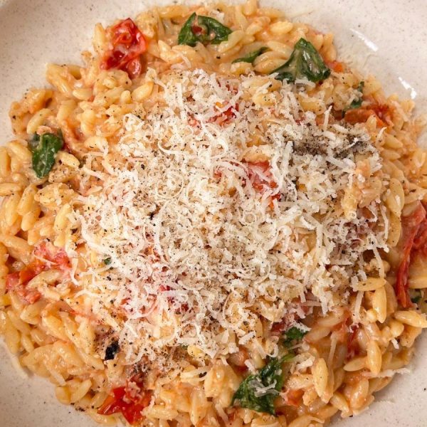 Bowl of tomato orzo with basil topped with grated parmesan.