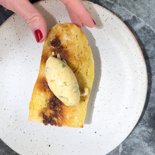 Woman with painted nails picking up a piece of toast with a piece of roasted garlic brown butter on the top.