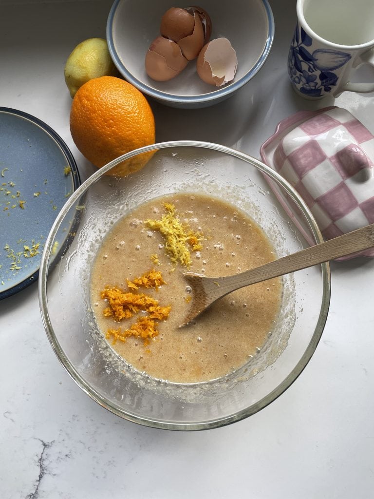 Adding orange and lemon zest to the cake mix in the glass mixing bowl