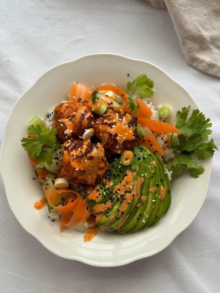 Bowl of fishcakes, rice, carrot, cucumber, avocado and coriander covered with a spicy mayonnaise and sesame seeds.