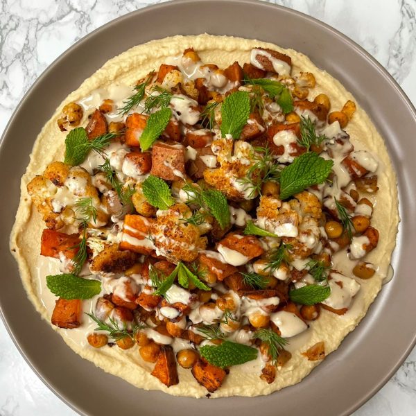 Plate of hummus topped with roasted cauliflower and sweet potato with herbs