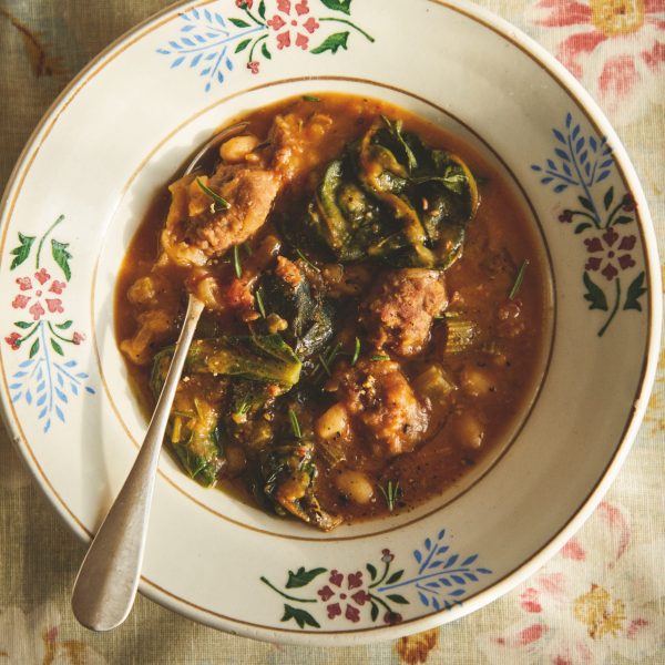 Vintage bowl of sausage and bean stew on a red floral tea towel.