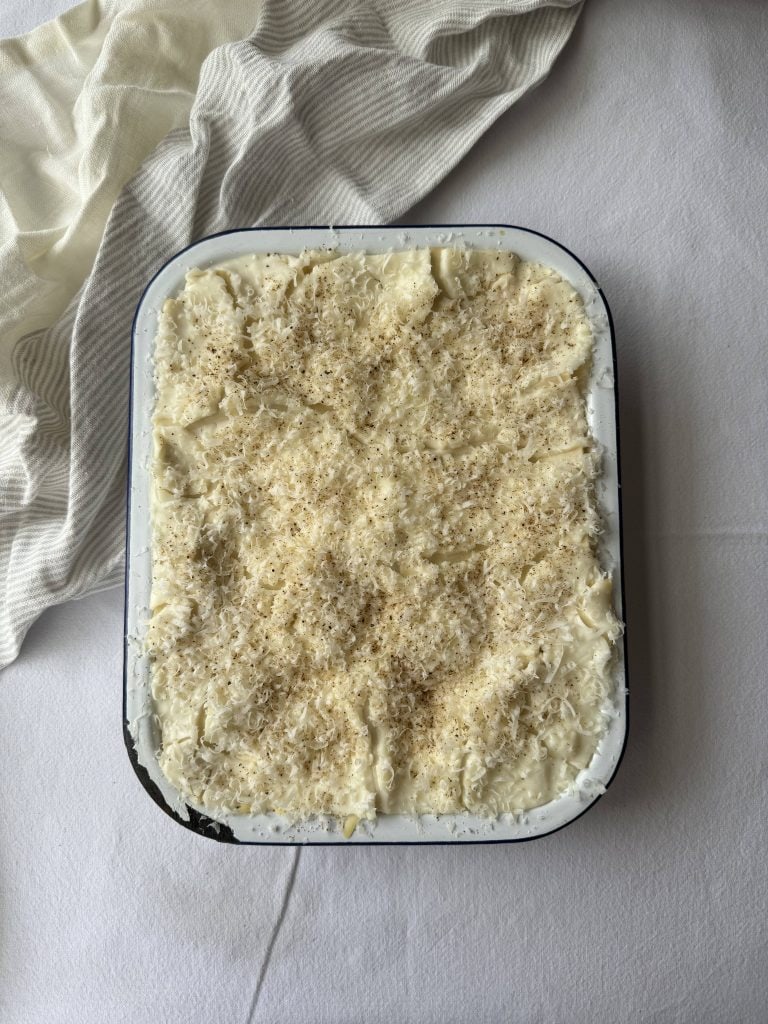 A rectangular dish of lasagne, before baking with grated cheese on top