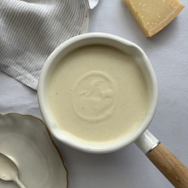 White sauce in a small white saucepan with parmesan on the side and a plate with a spoon