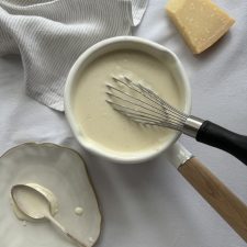 A whisk in a saucepan of creamy white sauce