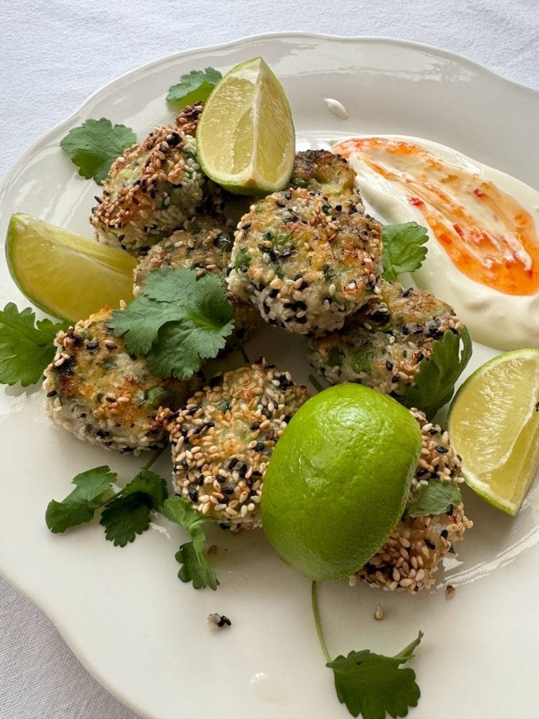 Plate of sesame seed coated fish cakes with fresh lime wedges.