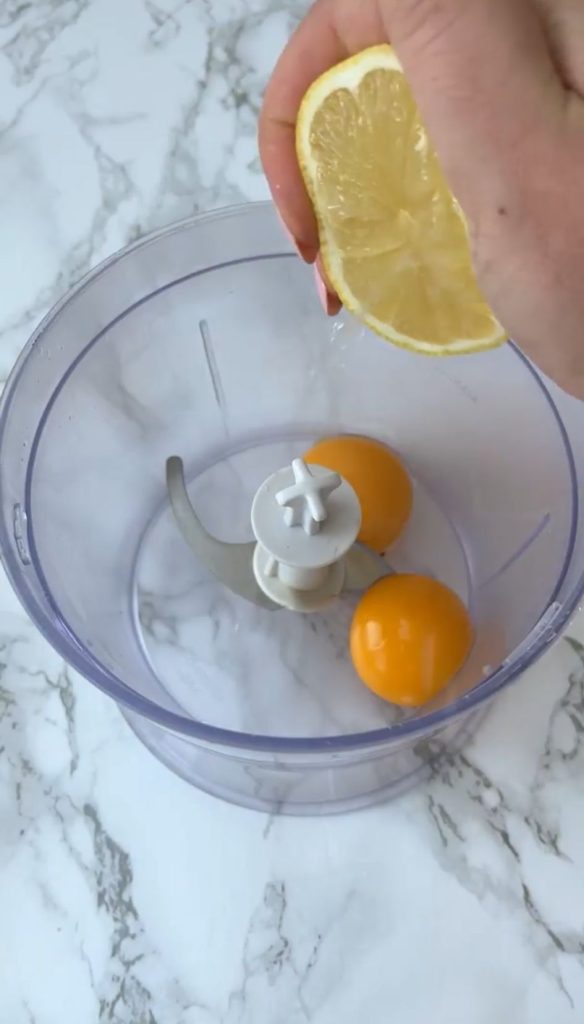 Two egg yolks in a blender, woman adding lemon juice