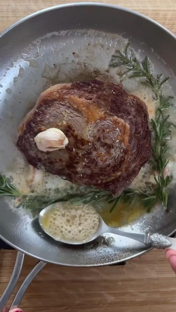 Woman basting the rib eye steak in rosemary garlic butter