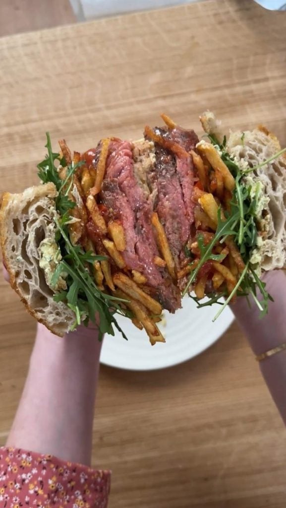 Woman holding a rib eye steak sandwich with chips, tomatoes, rocket, bearnaise butter