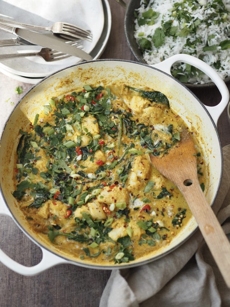 A cod and coconut curry with wilded spinach and red chilli in a white casserole dish.