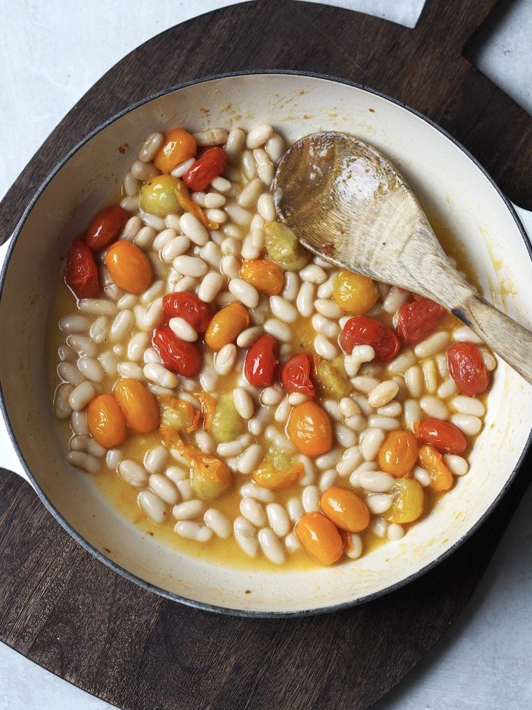 White beans and cherry tomatoes being cooked in a shallow casserole dish.