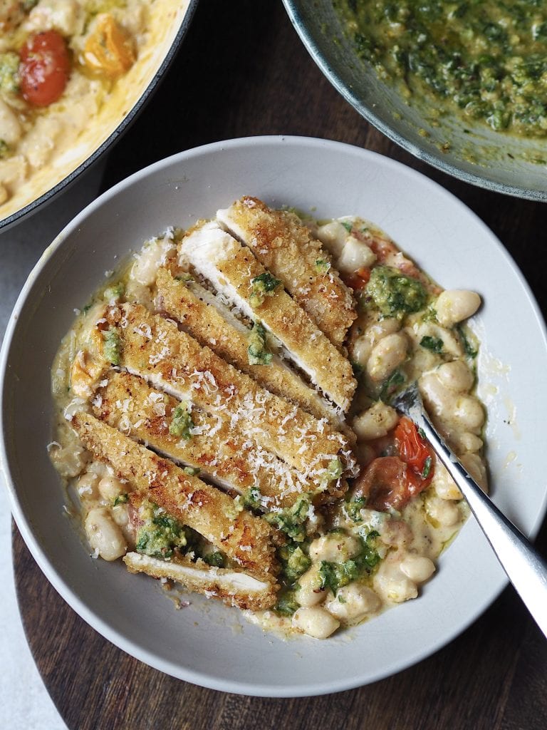 Grey bowl of white beans and cherry tomatoes topped with a sliced crispy chicken cutlet.