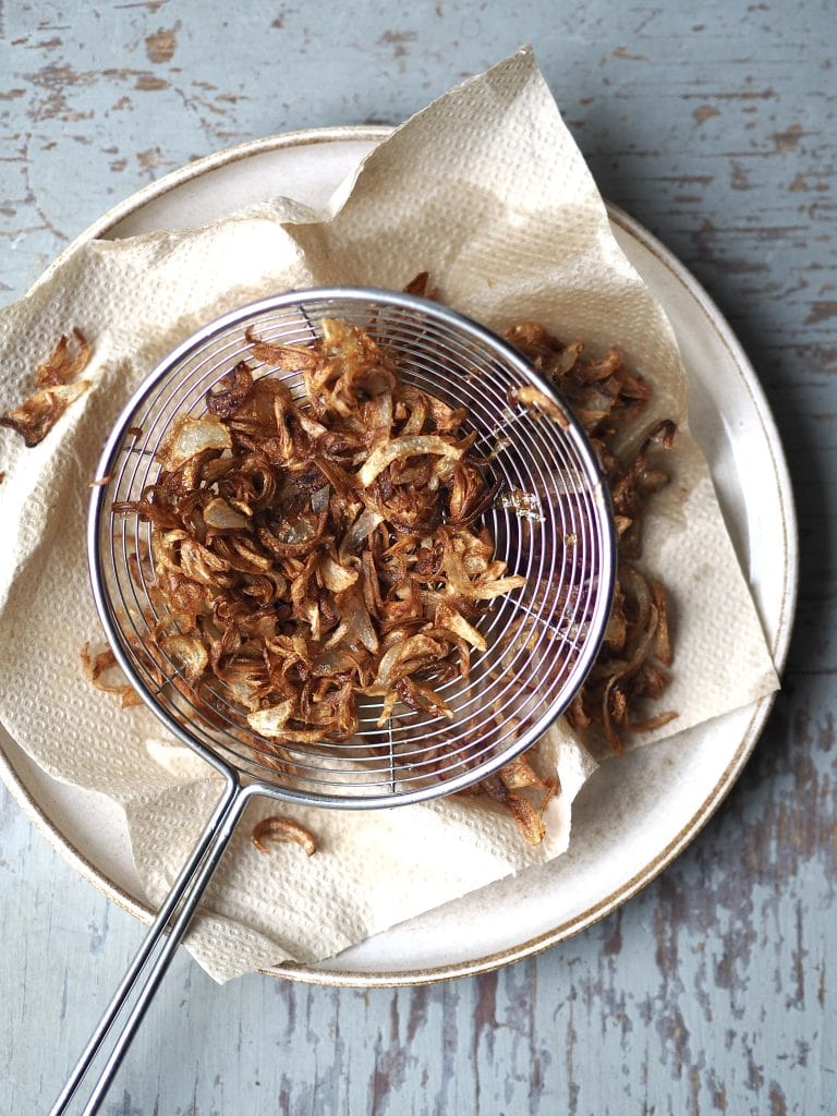 A plate with crispy shallots draining on kitchen paper.