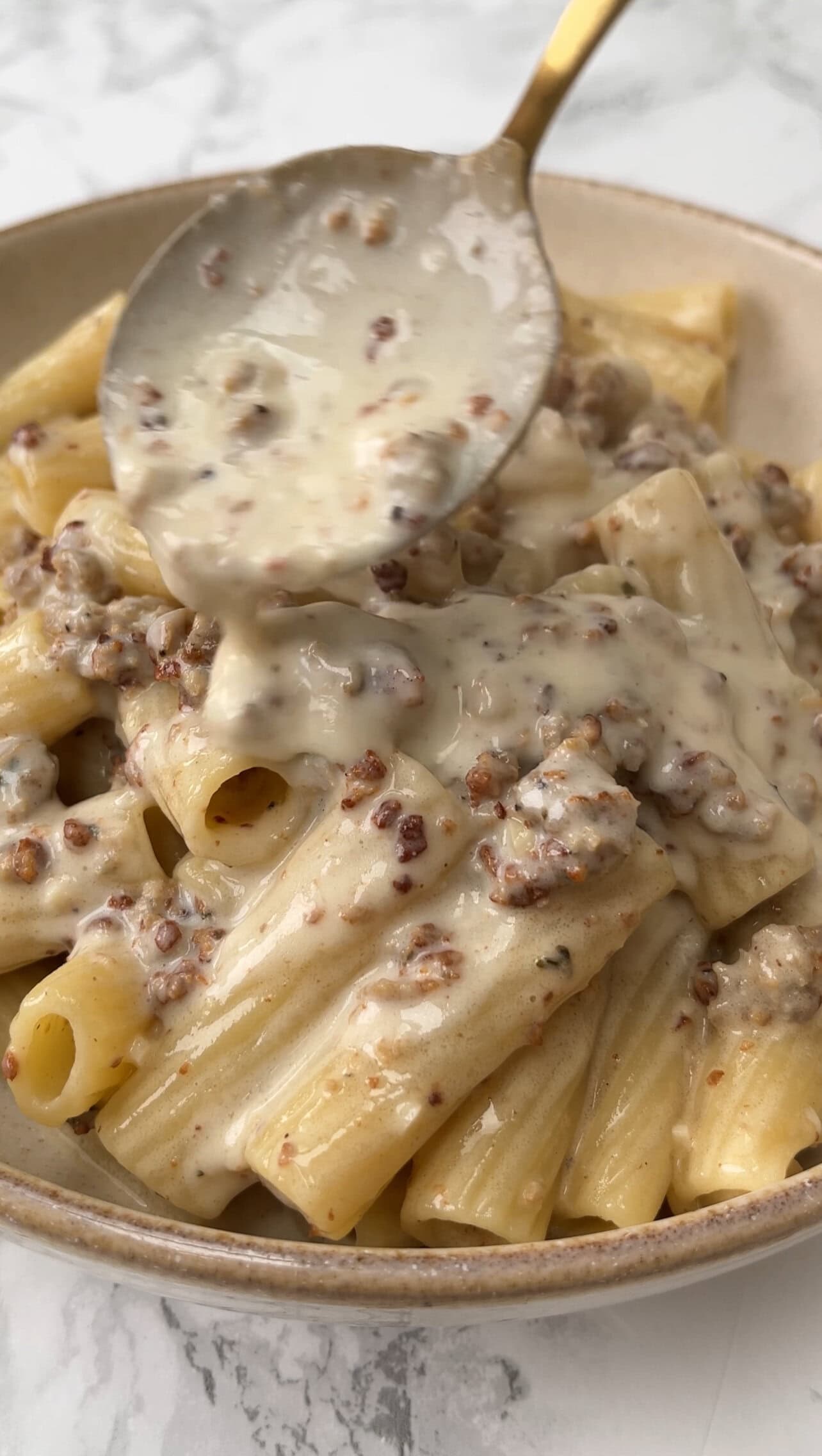 creamy sausage pasta in beige bowl, spooning sauce over.