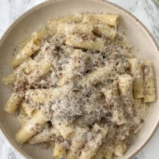 creamy sausage pasta in a beige bowl covered in a grating of cheese.
