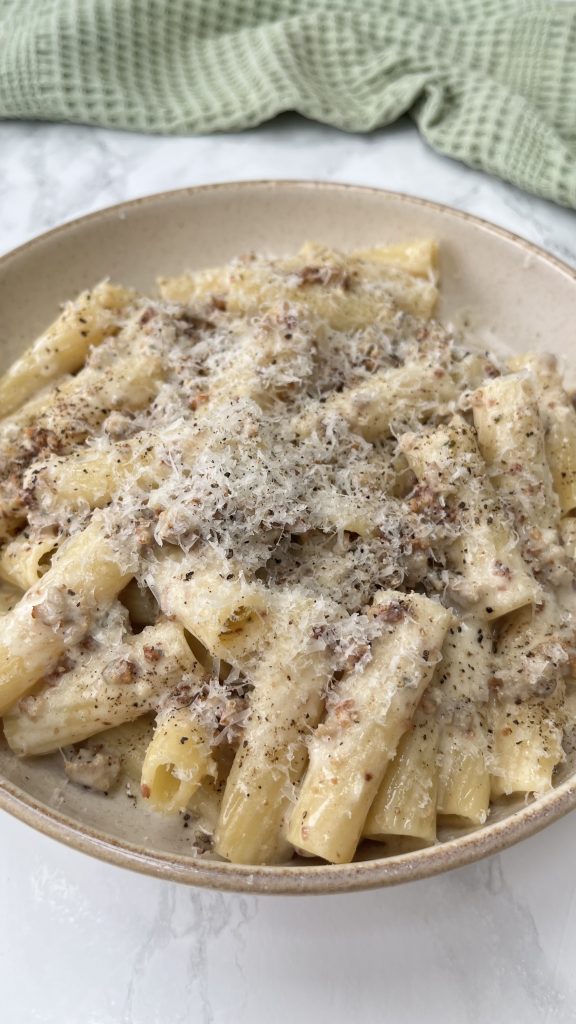 A close up of a bowl of creamy sausage rigatoni covered in cheese