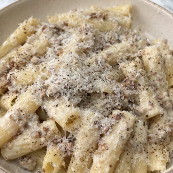 A close up of a bowl of creamy sausage rigatoni covered in cheese