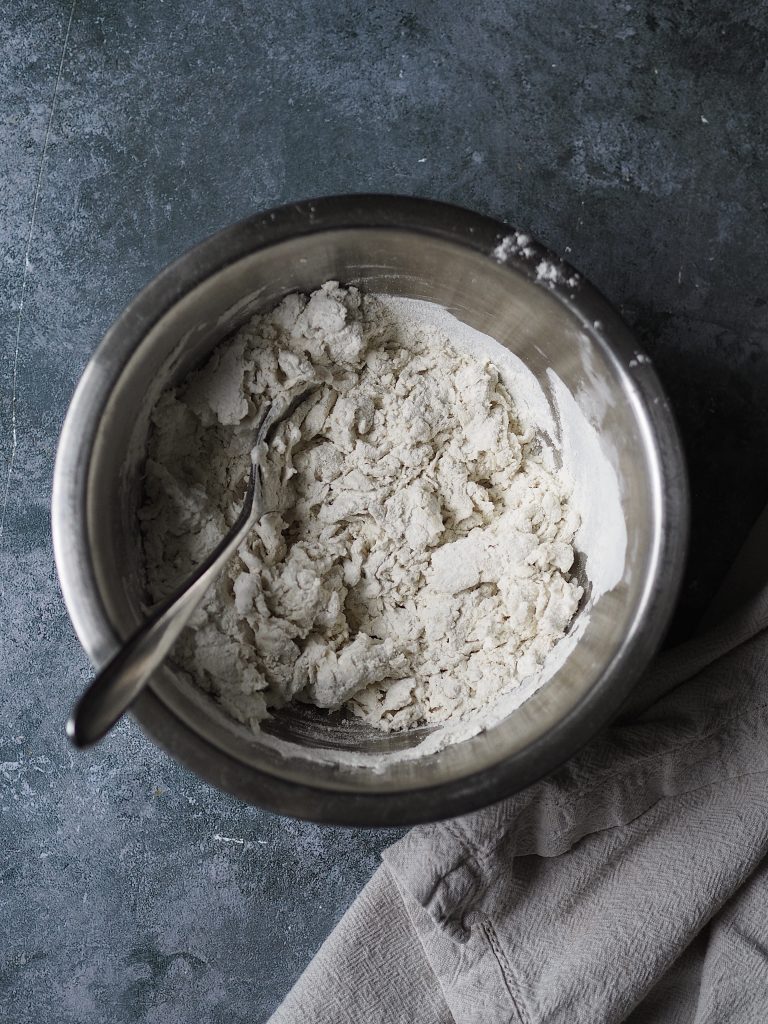 Metal bowl of flour being mixed with water using a fork.