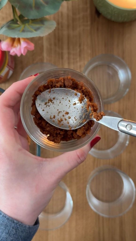 Woman holding a glass and using a spoon to pack in the cheesecake base