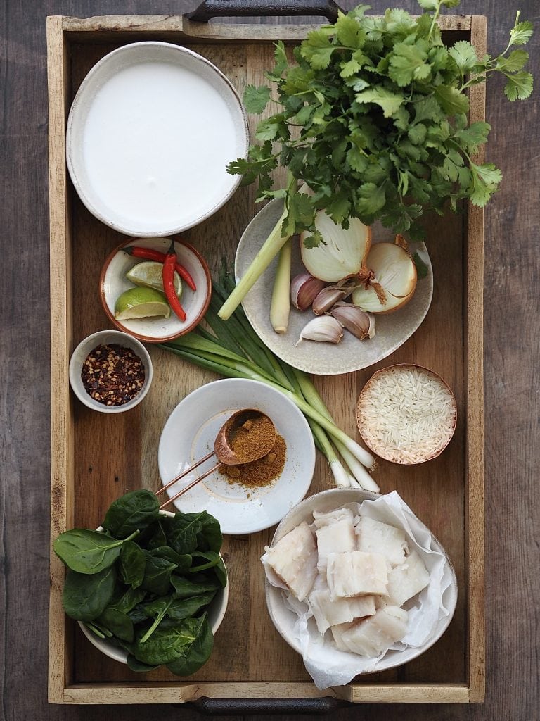 Ingredients to make a fish curry on a wooden tray.