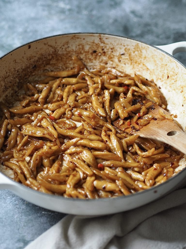 Shallow casserole dish of scissor cut noodles being tossed in chilli oil.