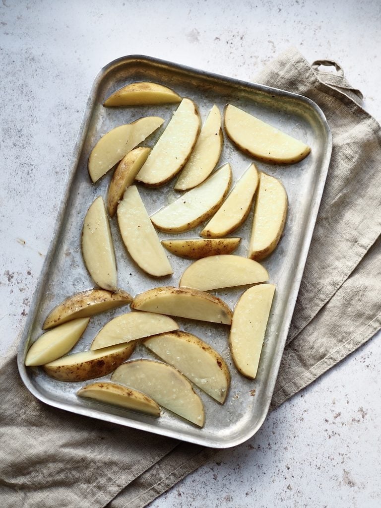 Tray of uncooked potato wedges tossed in olive oil.