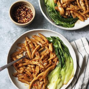 Two plates of scissor cut noodles in chilli oil with pak choi on the side.