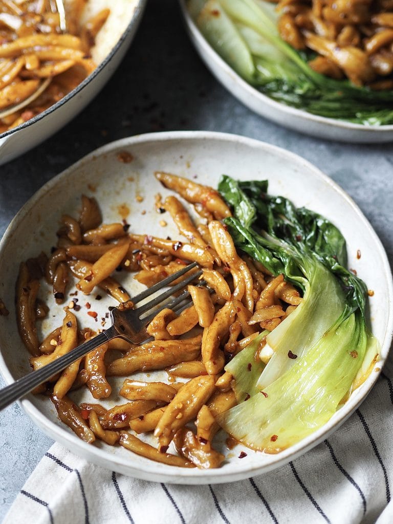 A half eaten bowl of spicy scissor-cut noodles with some wilted pak choi on the side.