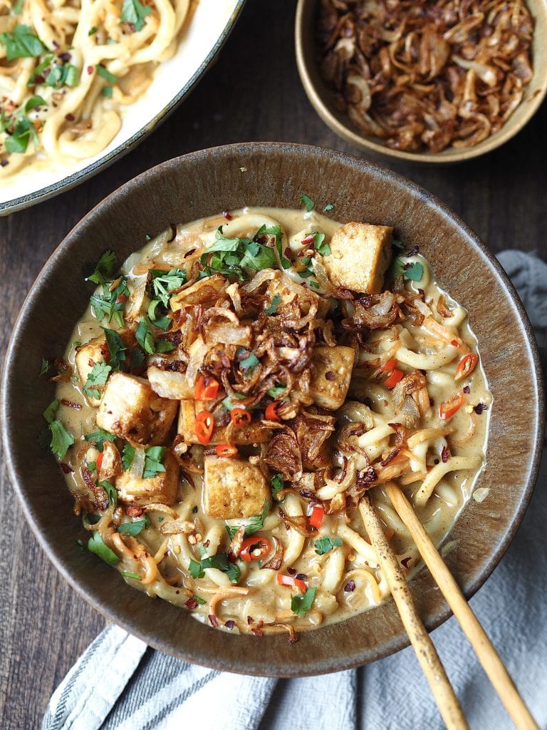 A bowl of curry udon topped with crispy shallots and tofu.