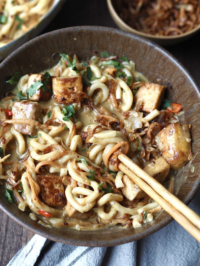 A bowl of curry udon soup being stirred withy chopsticks.