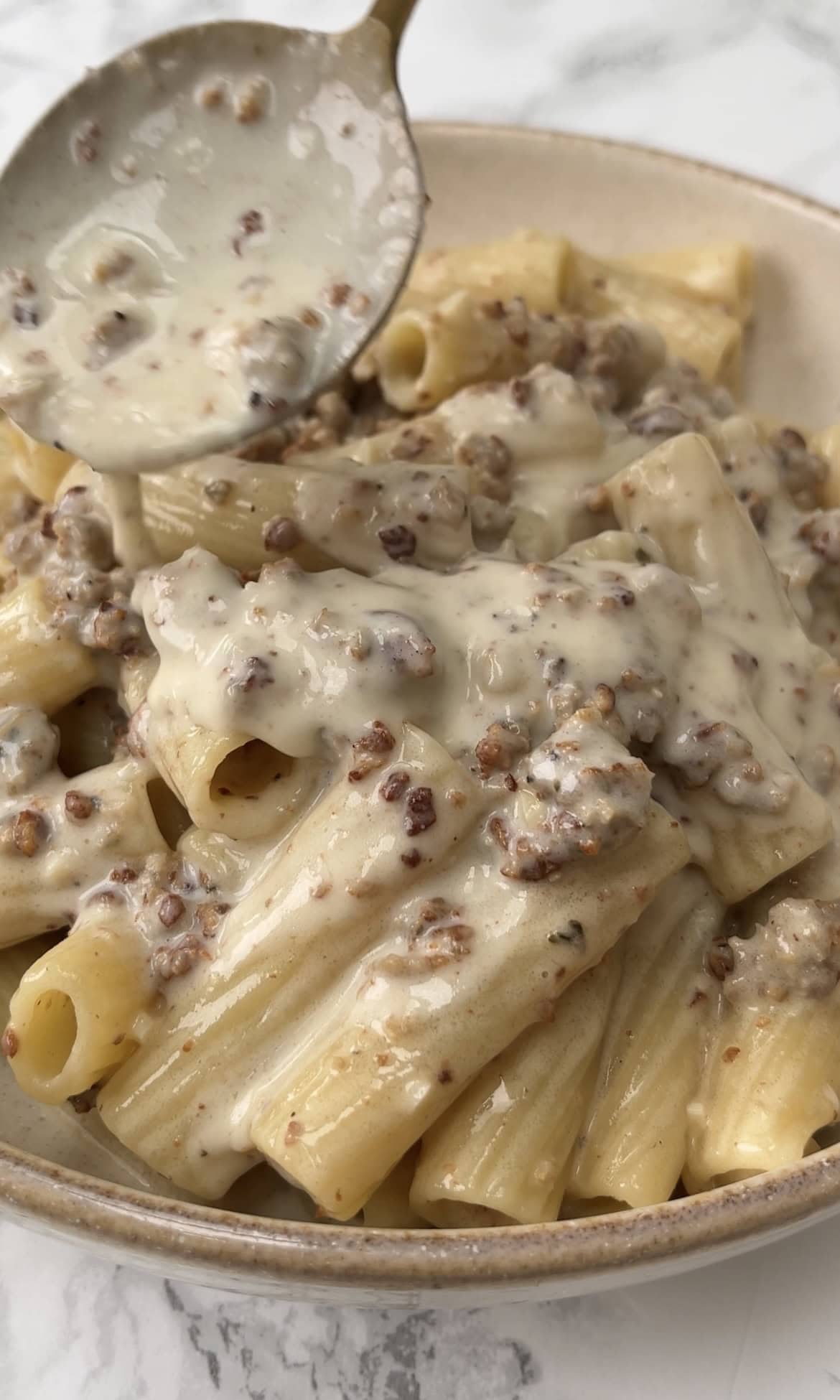 spooning sauce over creamy sausage pasta.