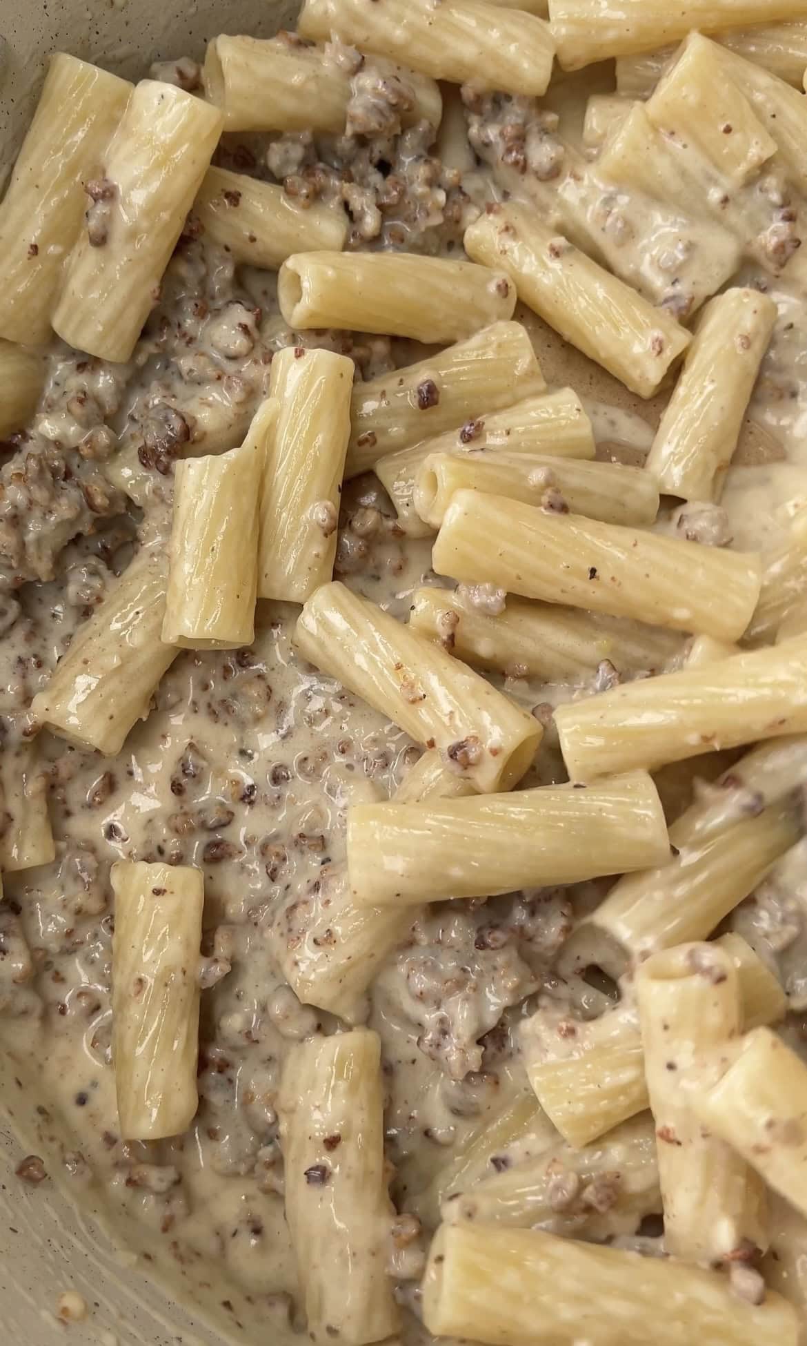 tossing creamy sausage pasta in pan.