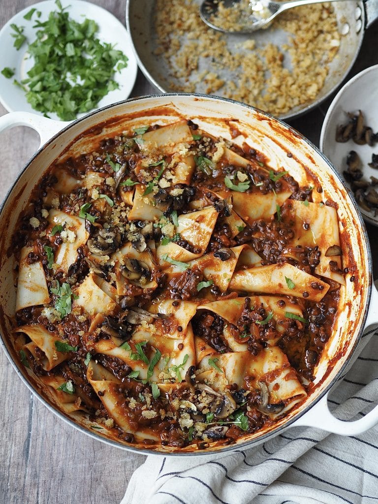 Lentil and mushroom bolognese with pasta and parsley in a shallow white casserole dish.