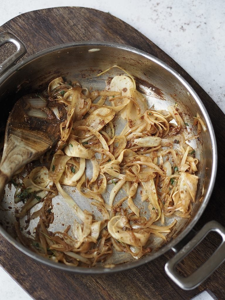 Sliced fennel and onions caramalised in a frying pan.