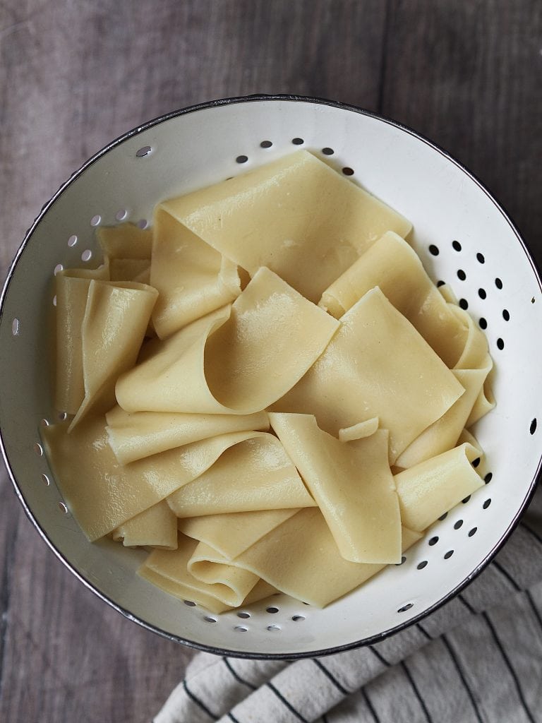 Cooked lasagne sheets in a white metal sieve.